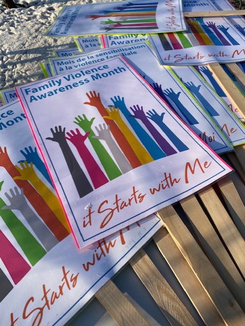 A sign with art work (many hands with different colours) that says: Family violence Awareness Month, it starts with me 